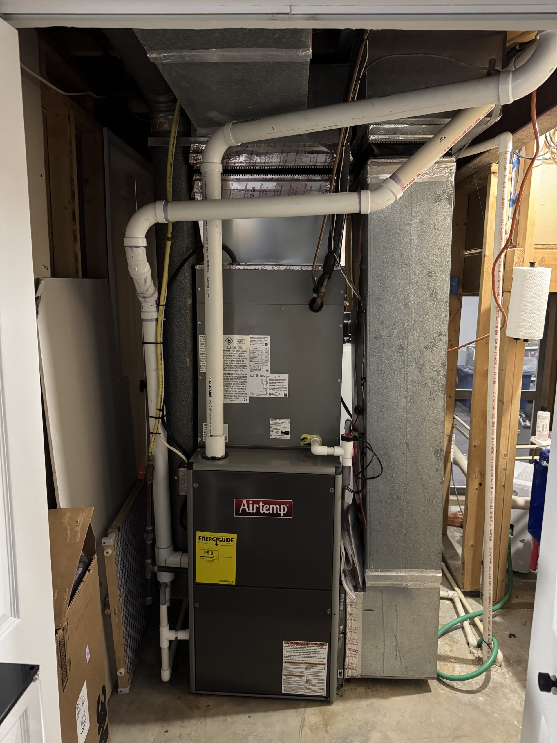 Residential HVAC furnace unit with pipes and ductwork in a utility closet; brand label Airtemp visible on the front panel.