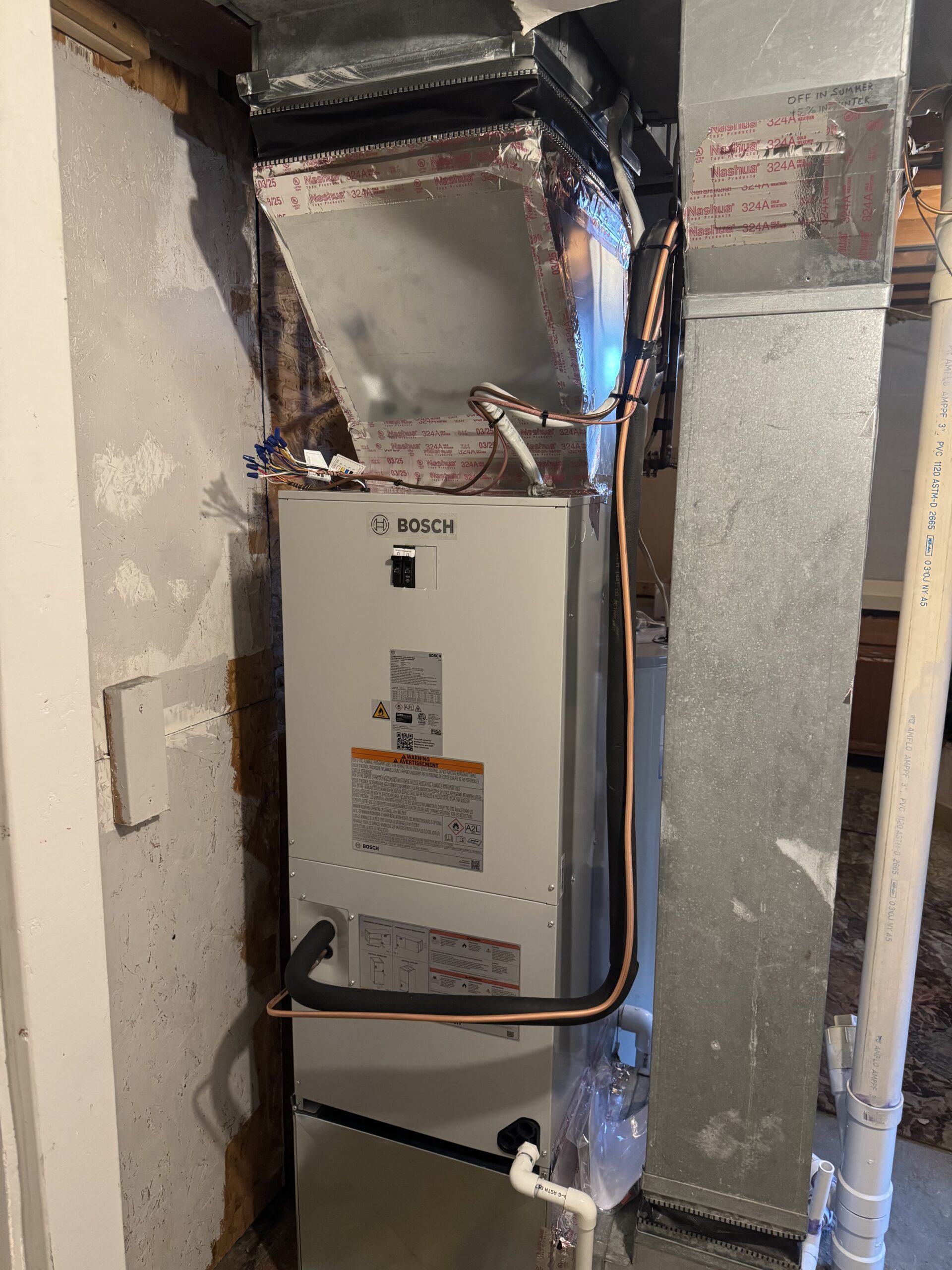 Bosch HVAC unit installed in a basement, connected to ductwork and electrical wiring, with pipes and insulation visible nearby.